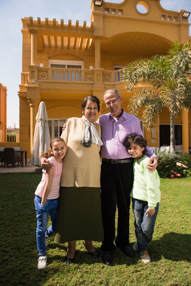 Grandparents and grandchildren smiling together outside their home